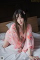 A woman in a pink kimono sitting on a bed.