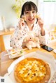 A woman sitting at a table with a pizza and a teddy bear.