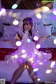 A woman in a white dress sitting on a bed covered in lights.