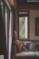 A naked woman sitting on a couch looking out a window.