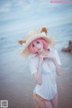 A woman with pink hair wearing a straw hat on the beach.