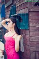 A woman in a pink dress leaning against a wooden wall.