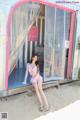 A woman sitting on a bench in front of a pink building.