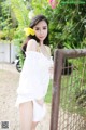 A woman in a white dress standing next to a fence.