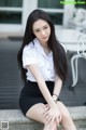 A woman in a white shirt and black skirt sitting on a bench.