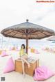 A woman in a yellow bathing suit sitting on a wooden bench under an umbrella.